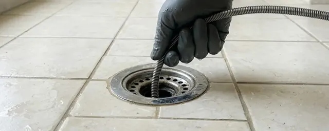 Gloved hand feeding a drain snake into a tiled floor drain