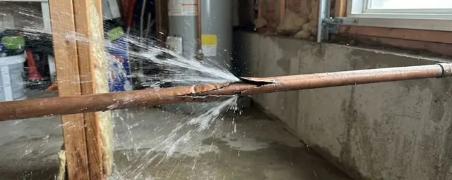 Split copper pipe spraying water in a basement