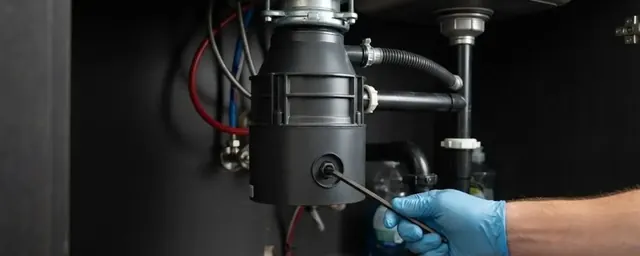 Gloved hand placing a hex key into the bottom of an under-sink garbage disposal