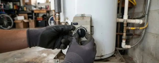 Gloved hands adjusting the thermostat dial on a tank water heater