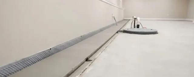Finished basement floor with a perimeter drain channel and a covered sump basin